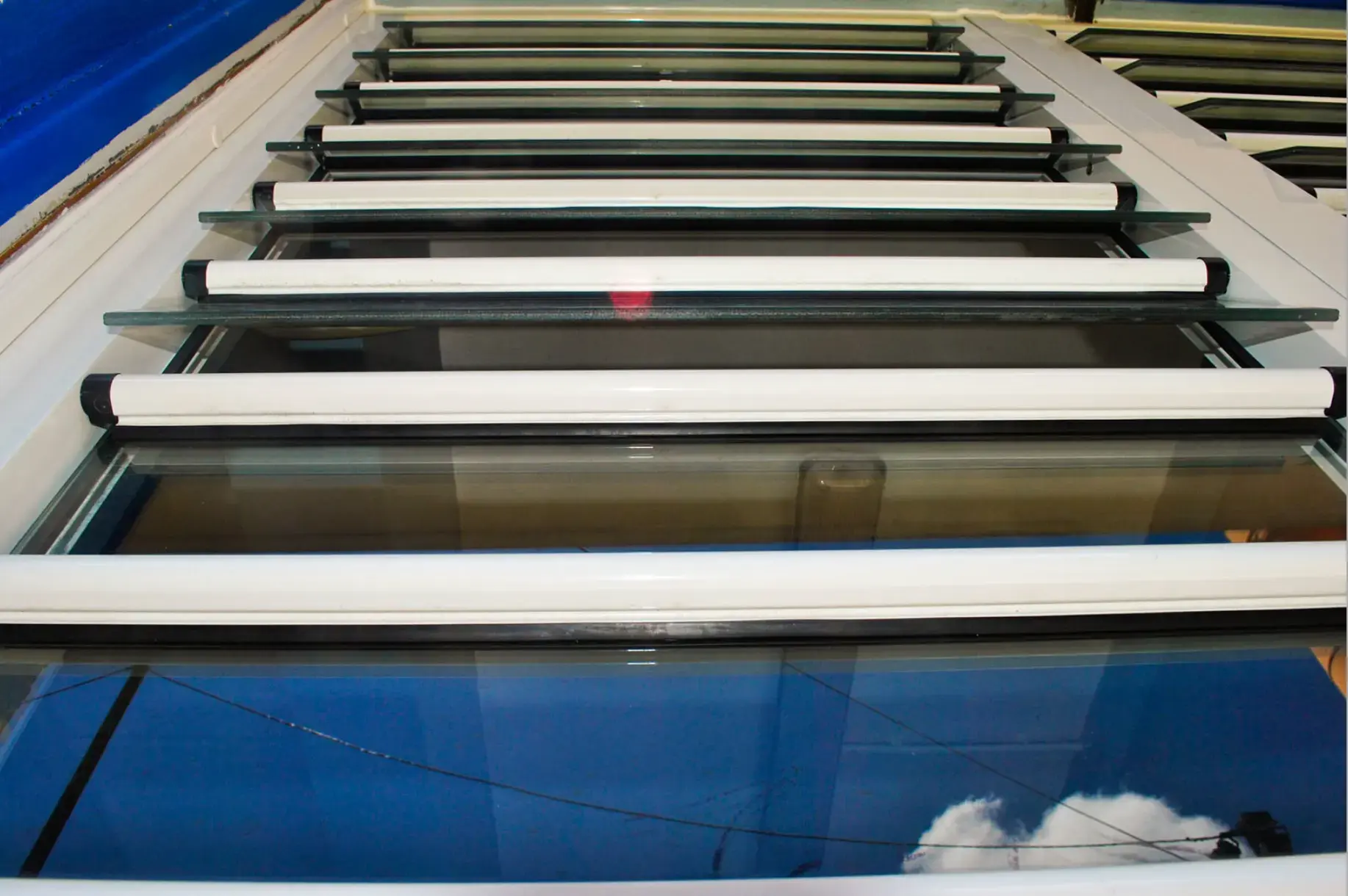 Détail d'une jalousie en aluminium, lames de verre et poignées blanches