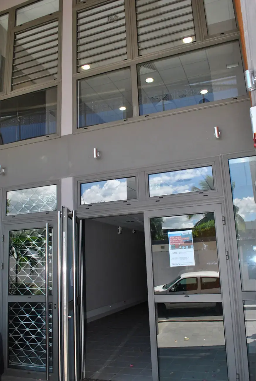 Entrée vitrée d'un bâtiment professionnel en aluminium, avec jalousies en imposte