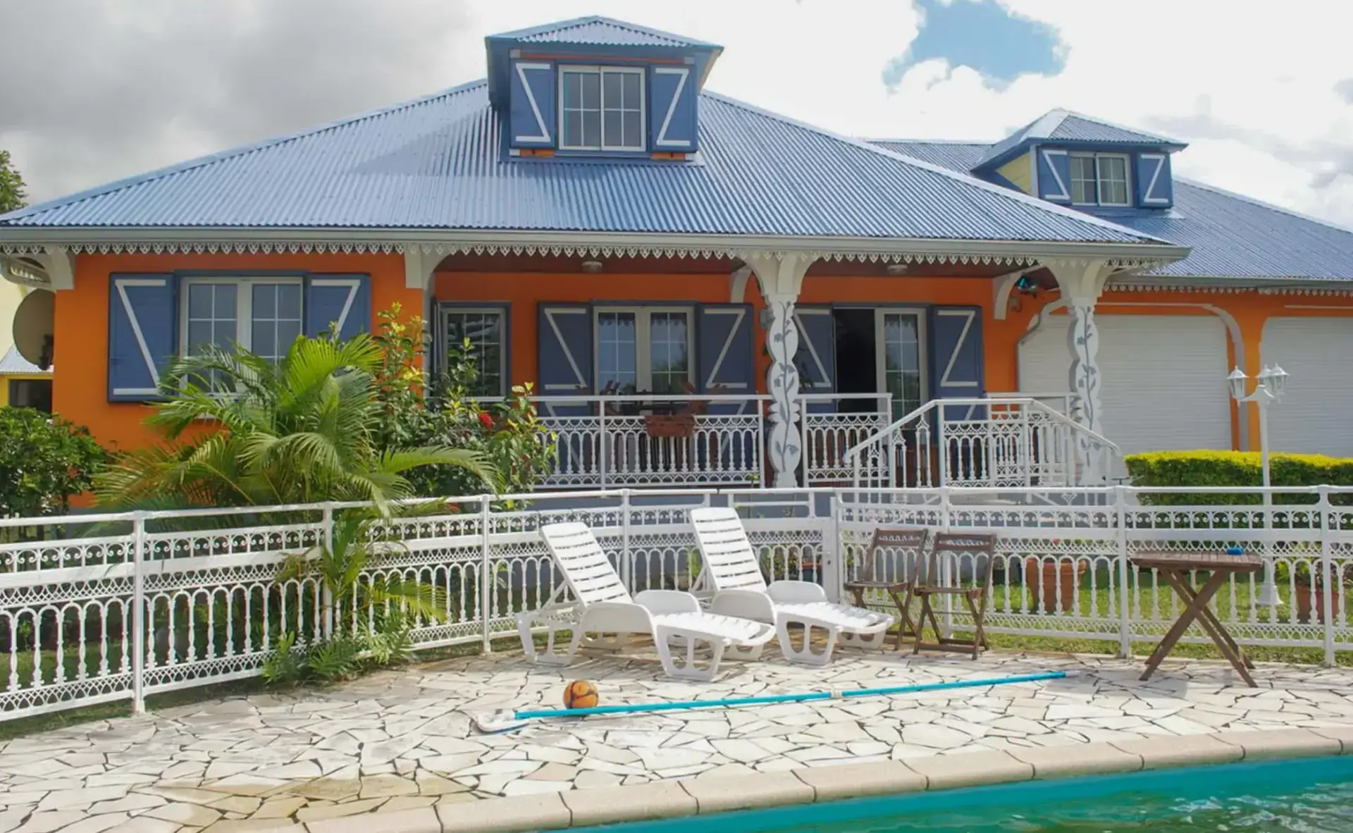 Villa créole avec volets battants bleus, garde-corps blanc et volet roulant en aluminium